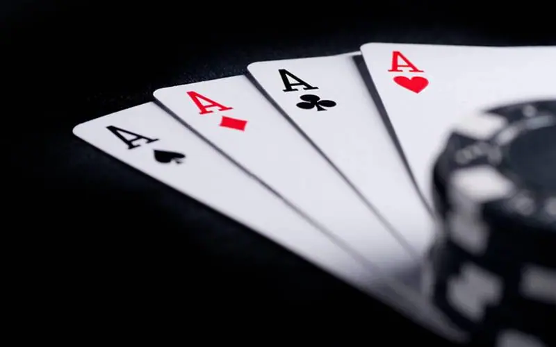 Four aces fanned on a dark table next to a stack of black casino chips