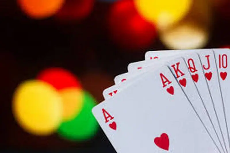 Royal flush hati, dari as sampai sepuluh, dipegang di depan lampu warna-warni yang buram